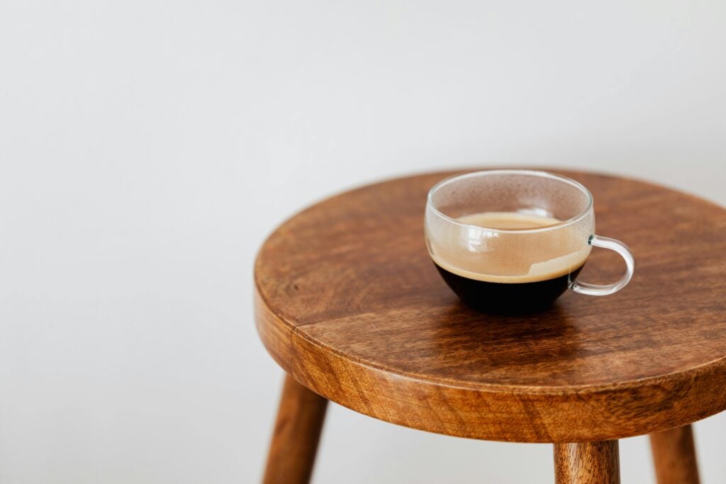 A glass cup of coffee on a wooden stool.
